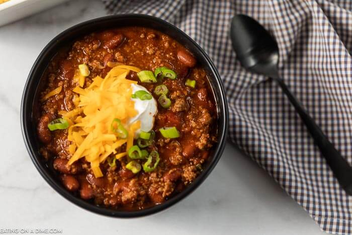 close up image of chili in a black bowl with a spoon and a dish towel. 