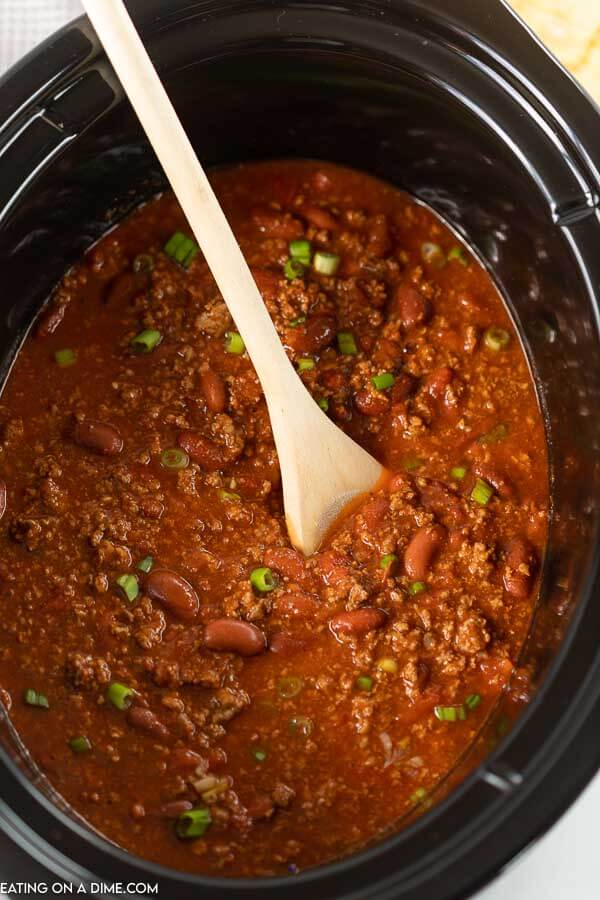 Close up image of chili in a crock pot with a wooden spoon. 