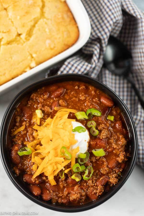 Close up image of chili in a black bowl topped with cheese, sour cream, and green onions. 