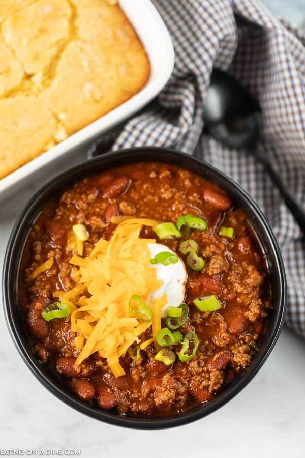 Close up image of a chili in a black bowl topped with cheese, sour cream and green onions. 