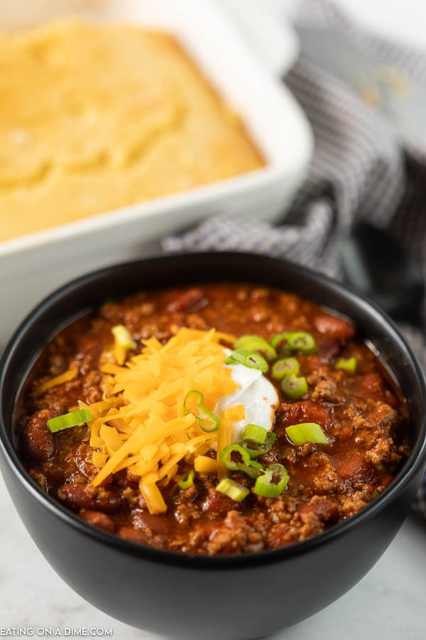 Close up image of chili in a black bowl topped with cheese, sour cream and green chilis. 