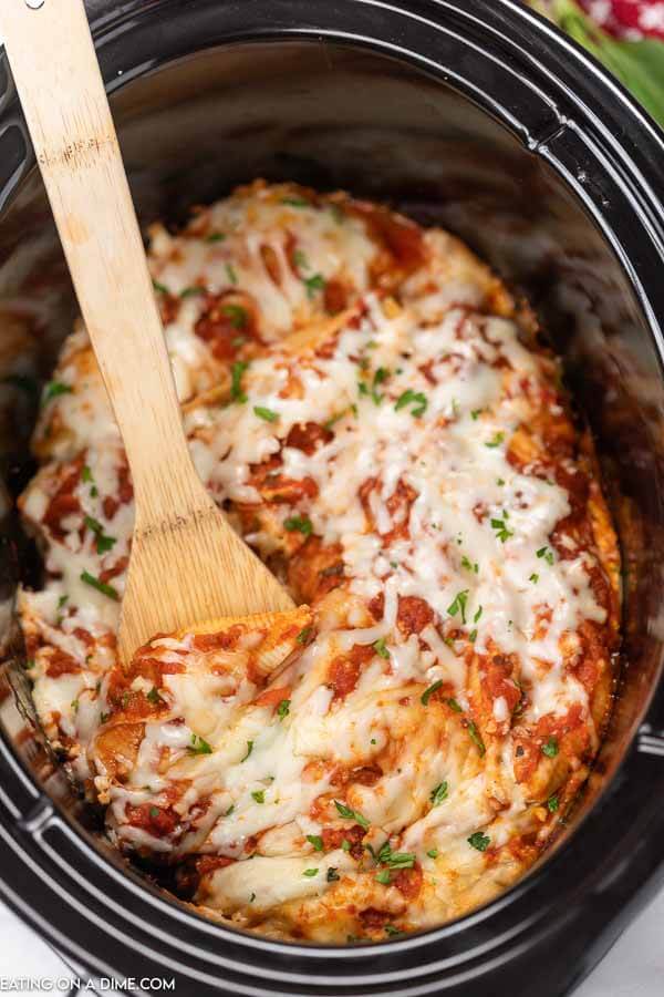 Close up image of stuffed shells in the slow cooker with a serving on a wooden spoon