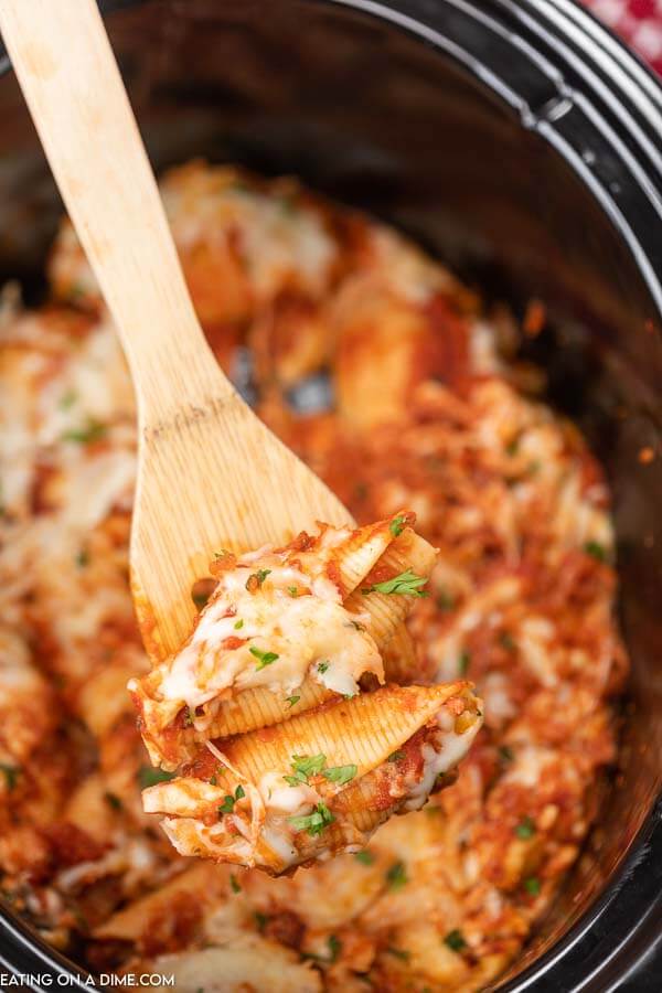 Close up image of stuffed shells in the slow cooker with a serving on a wooden spoon