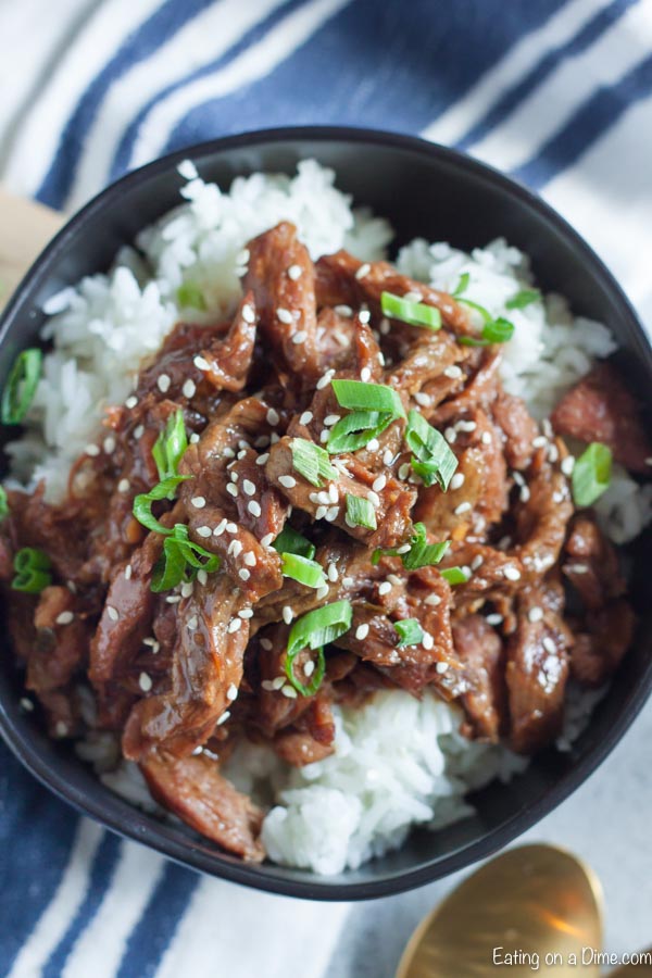 Close up image of sesame beef on rice in a black bowl.