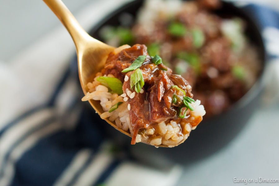 Close up image of a serving of sesame beef with rice on a wooden spoon.