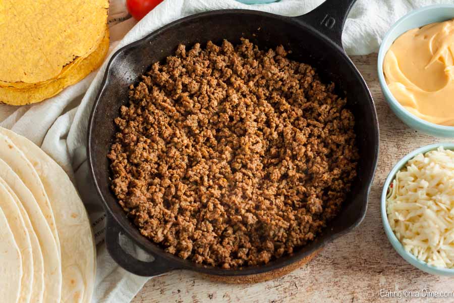 Skillet of ground beef with bowls of cheese, and stacks of tortillas