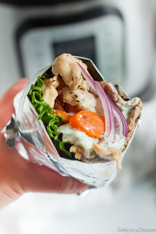 Close up image of chicken gyro with carrots and lettuce and some tzatziki sauce. Wrapped in foil.