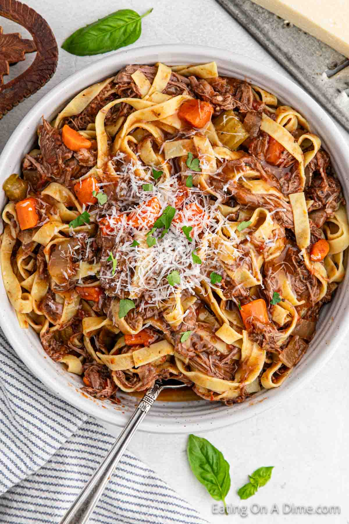 Close up image of beef ragu in a bowl topped with parmesan cheese