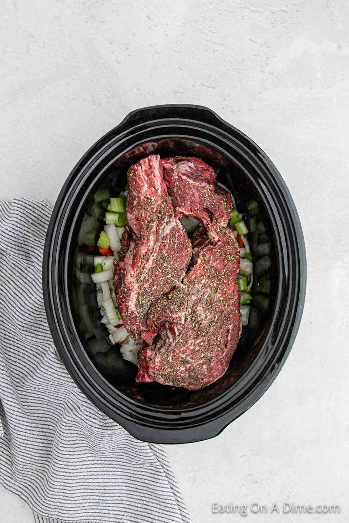 Placing the beef in the crock pot with the chopped veggies