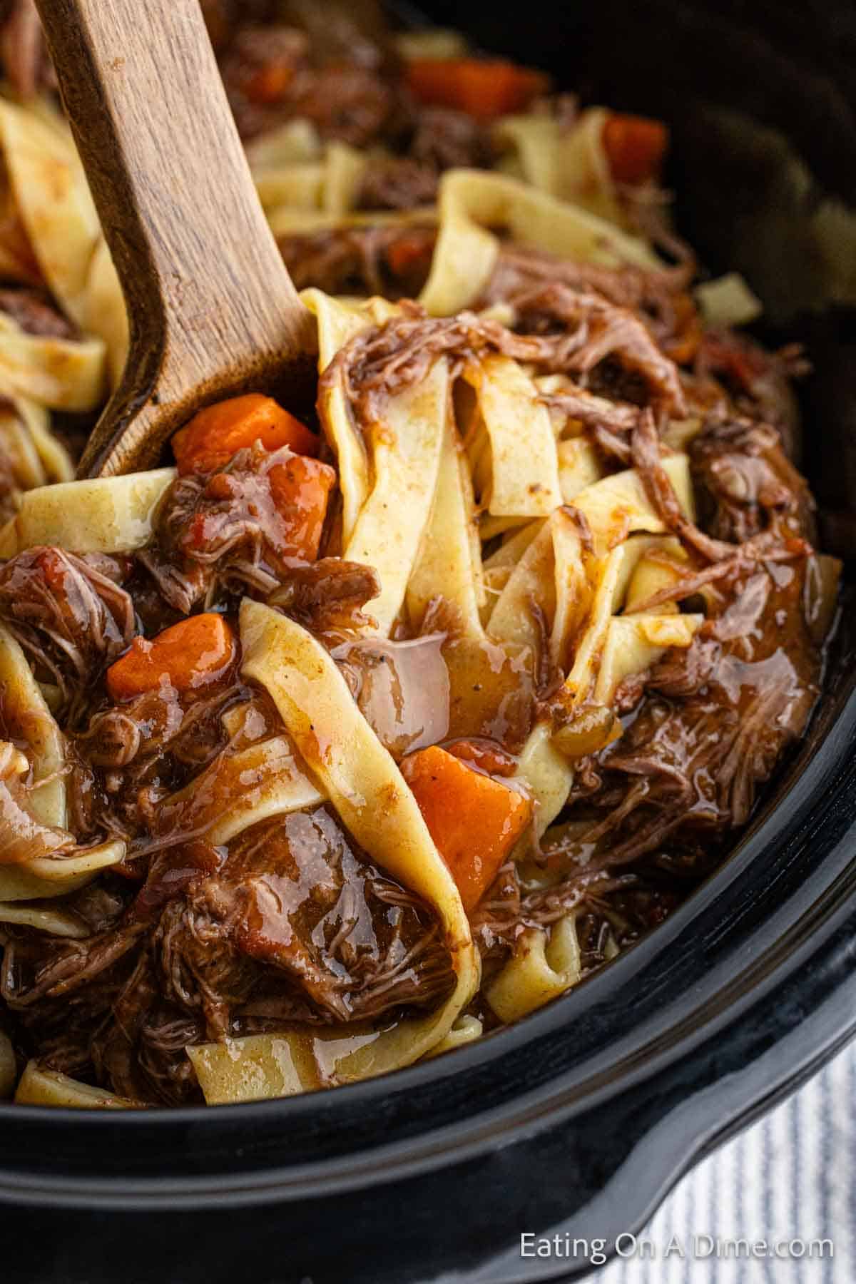 Close up image of beef ragu in the crock pot with a serving on a wooden spoon