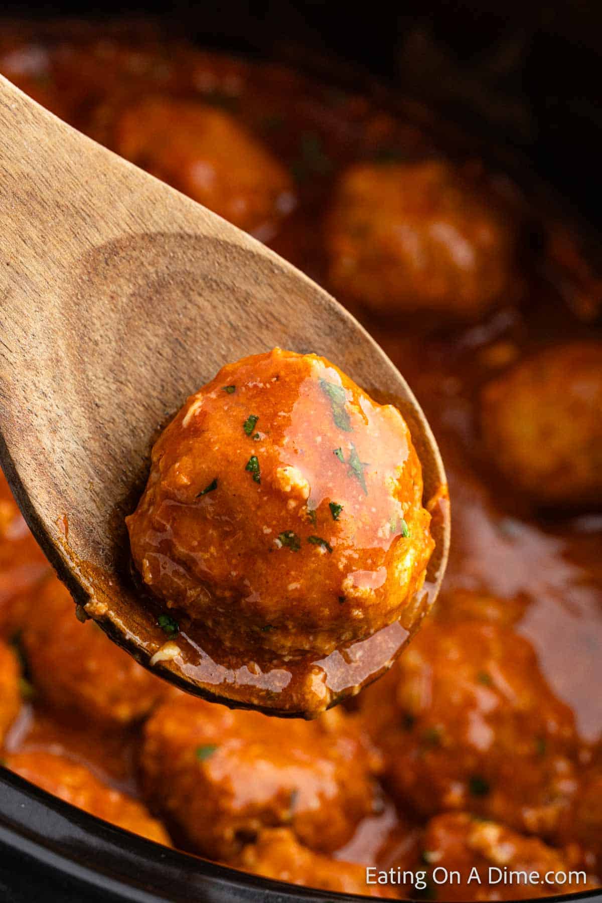 Buffalo Chicken Meatballs in the slow cooker with a serving on a wooden spoon