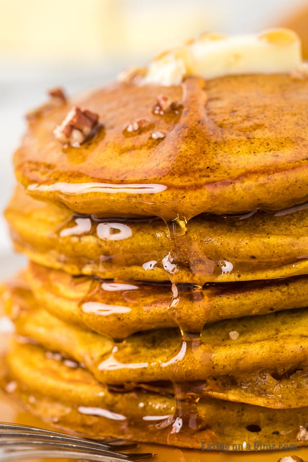 Close up image of stacked pumpkin pancakes with syrup and chopped pecans. 