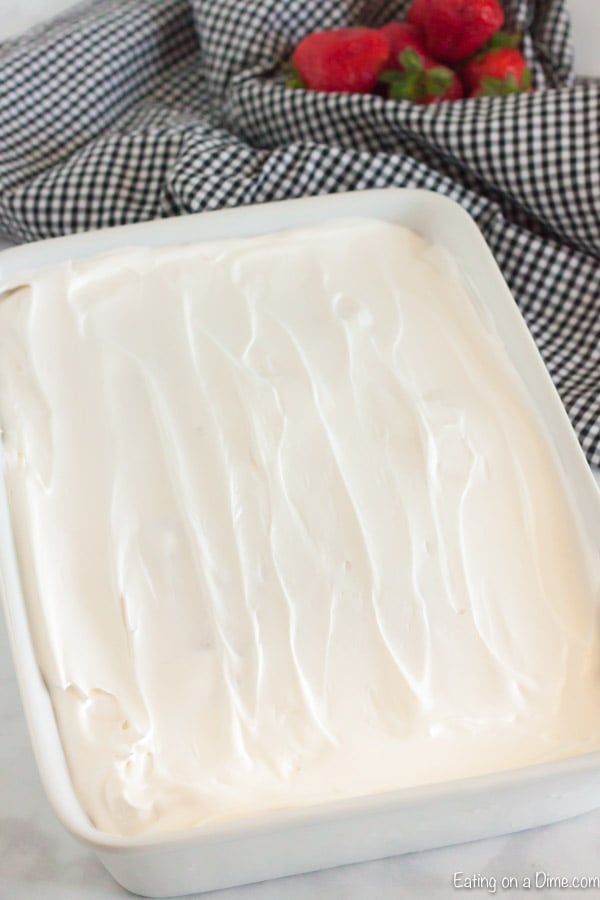 Close up image of strawberry jello cake with a whipped topping in a cake pan. 