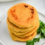 A stack of four golden-brown arepas sits on a white plate, garnished with a sprig of fresh cilantro on the side. This inviting arepas recipe promises crispy outsides and a soft, fluffy inside.