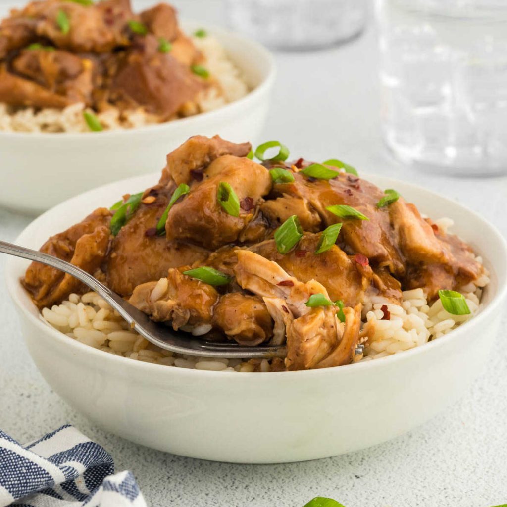 Bourbon Chicken in a bowl over rice with a fork