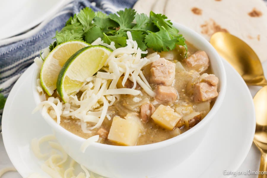 Close up image of green chili pork stew in a white bowl on a white plate. 