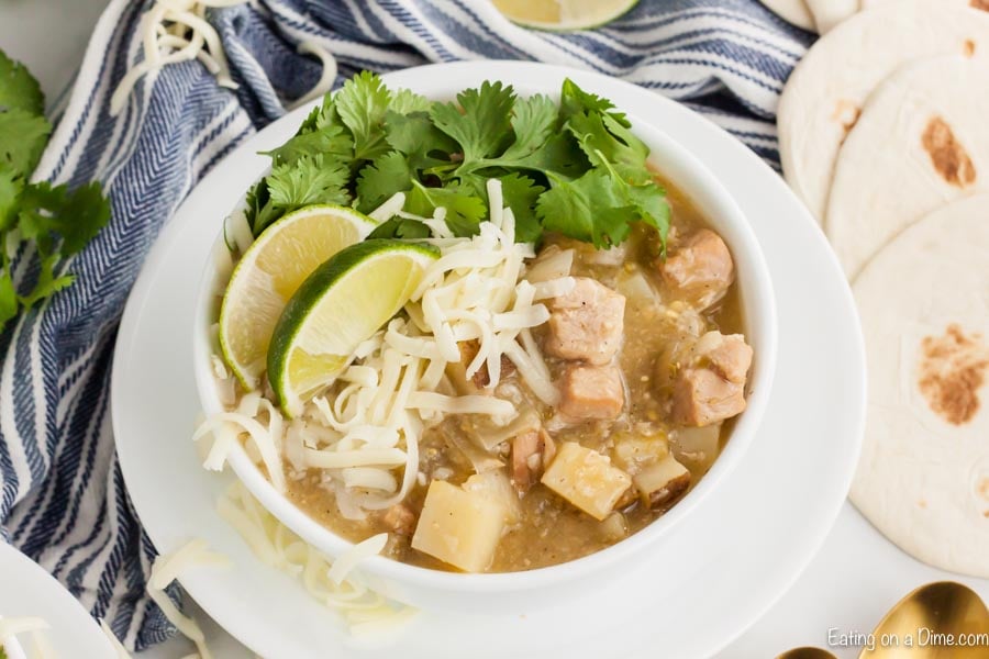 Close up image of green chili pork stew in a white bowl on a white plate. 