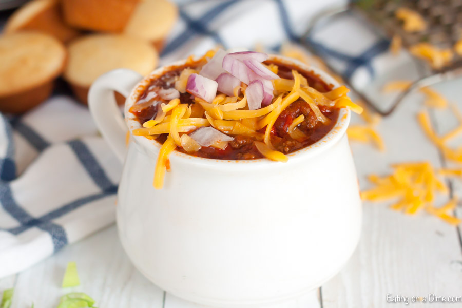 A black bowl of cowboy chili topped with sour cream, shredded cheese and red onions.  