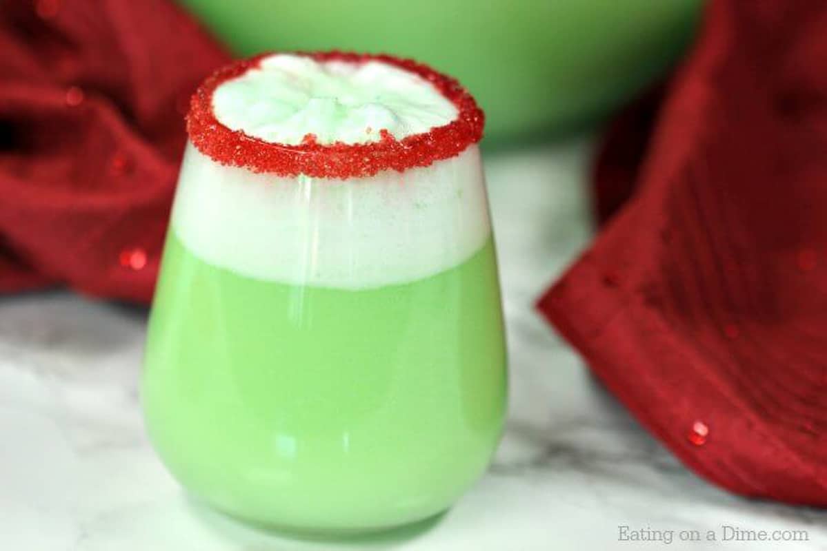 Close up image grinch punch in glass with red sprinkles on the glass. sitting in front of the grinch punch bowl