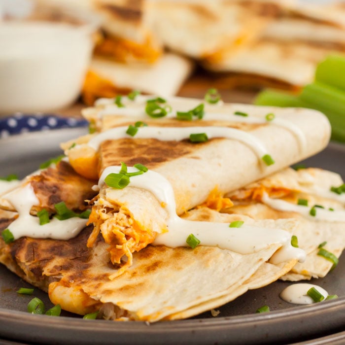 Buffalo Chicken Quesadilla slice with sour cream and green onions on a black plate