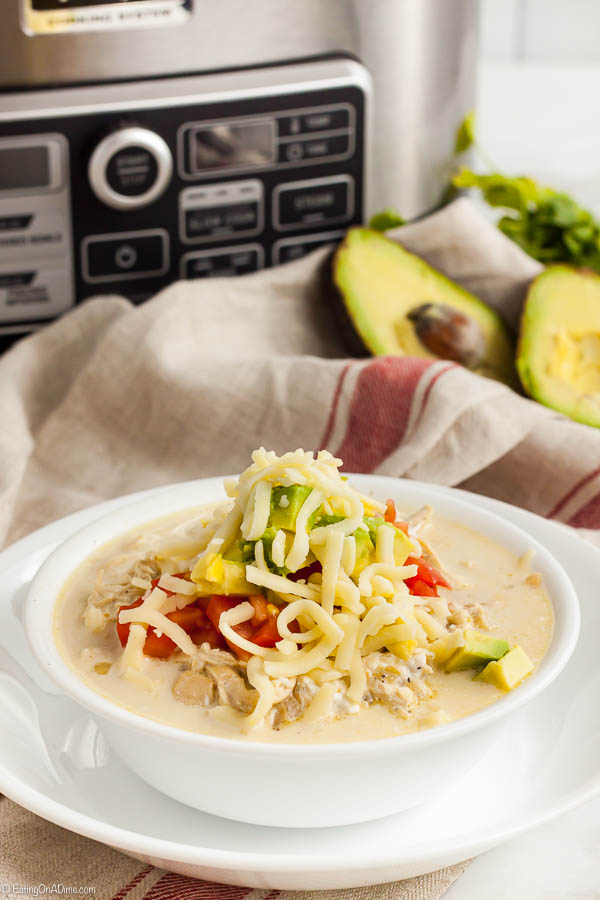 A bowl of Keto White Chicken Chili in front of a crock pot with extra avocados behind it. 