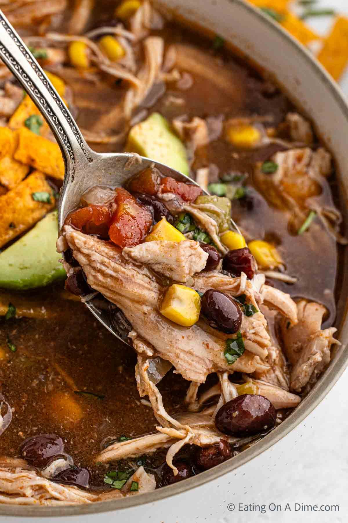 Bowl of Chicken Enchilada Soup topped with slice avocados and tortilla chips with a close up image of a serving on a spoon