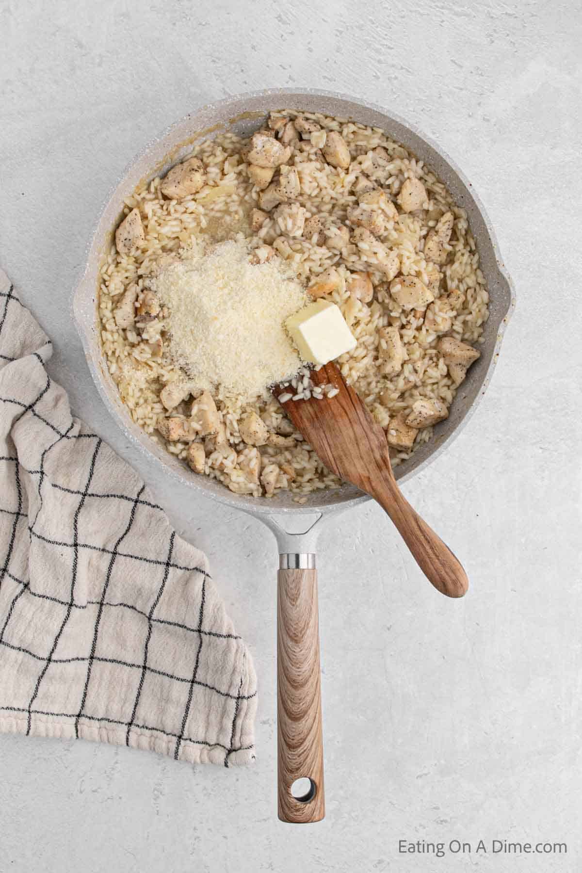 Adding in parmesan and butter to the cooked risotto and chicken in a skillet