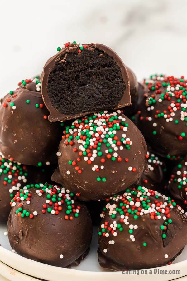 Oreo Balls with red, green and white sprinkles stacked on top of each other with a bite taken out of the top one so you can see the oreo mixture inside.  