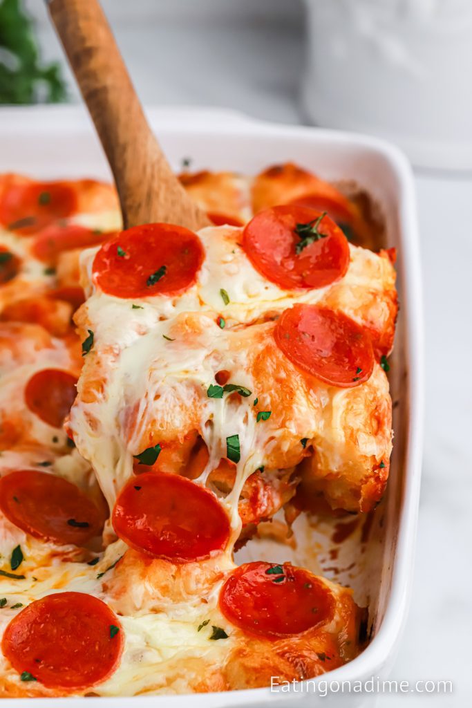 Bubble up pizza in a baking dish with a serving on a wooden spoon