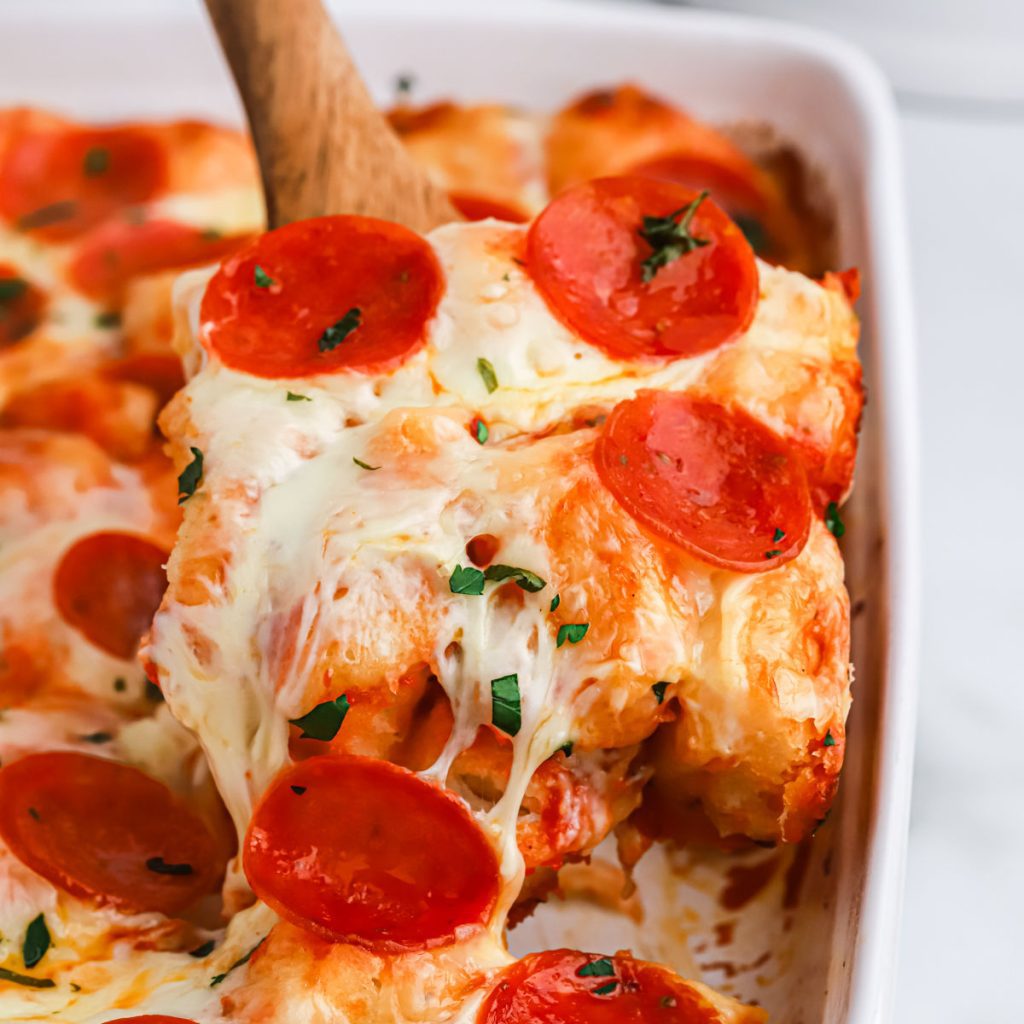 Bubble up pizza in a baking dish with a serving on a wooden spoon