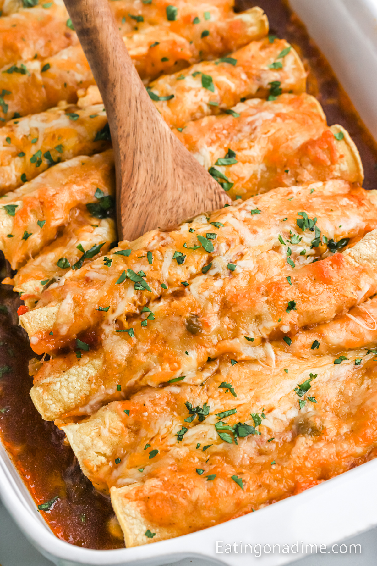 Shredded beef enchiladas in a baking dish with a wooden spoon