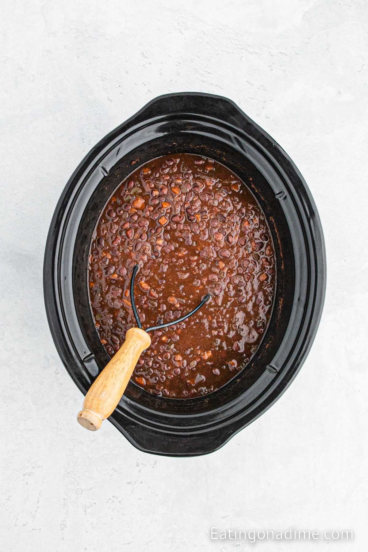 Black beans in soup in a slow cooker with a masher