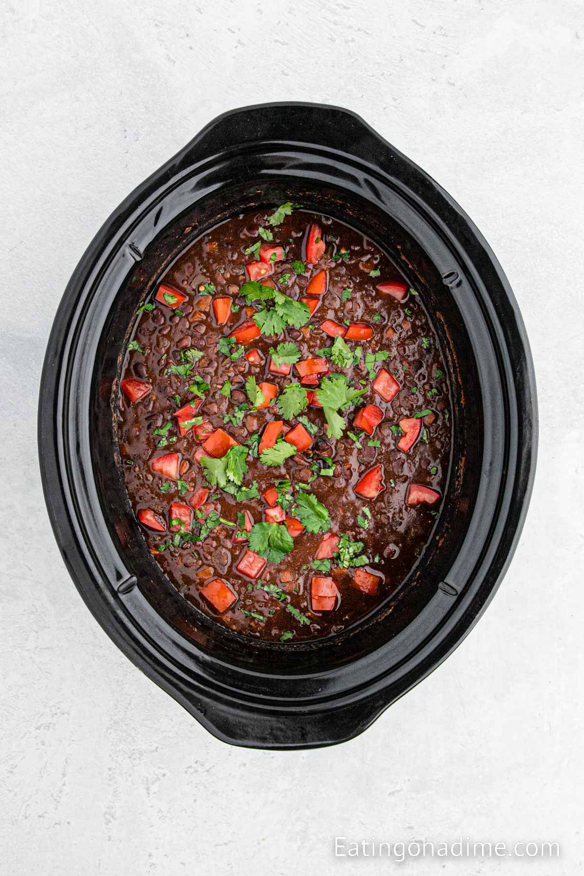 Black beans soup in a slow cooker topped with diced tomatoes and cilantro