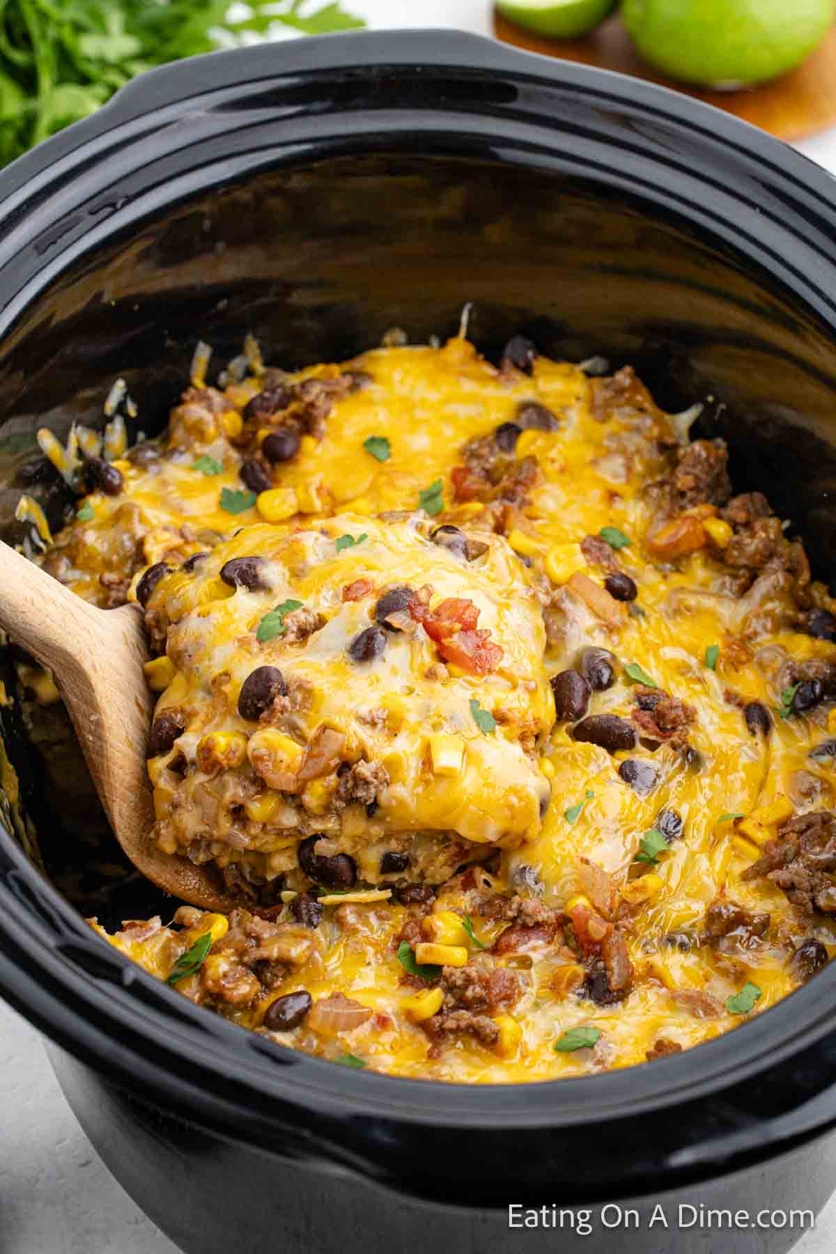 Mexican Lasagna in the slow cooker with a serving on a wooden spoon