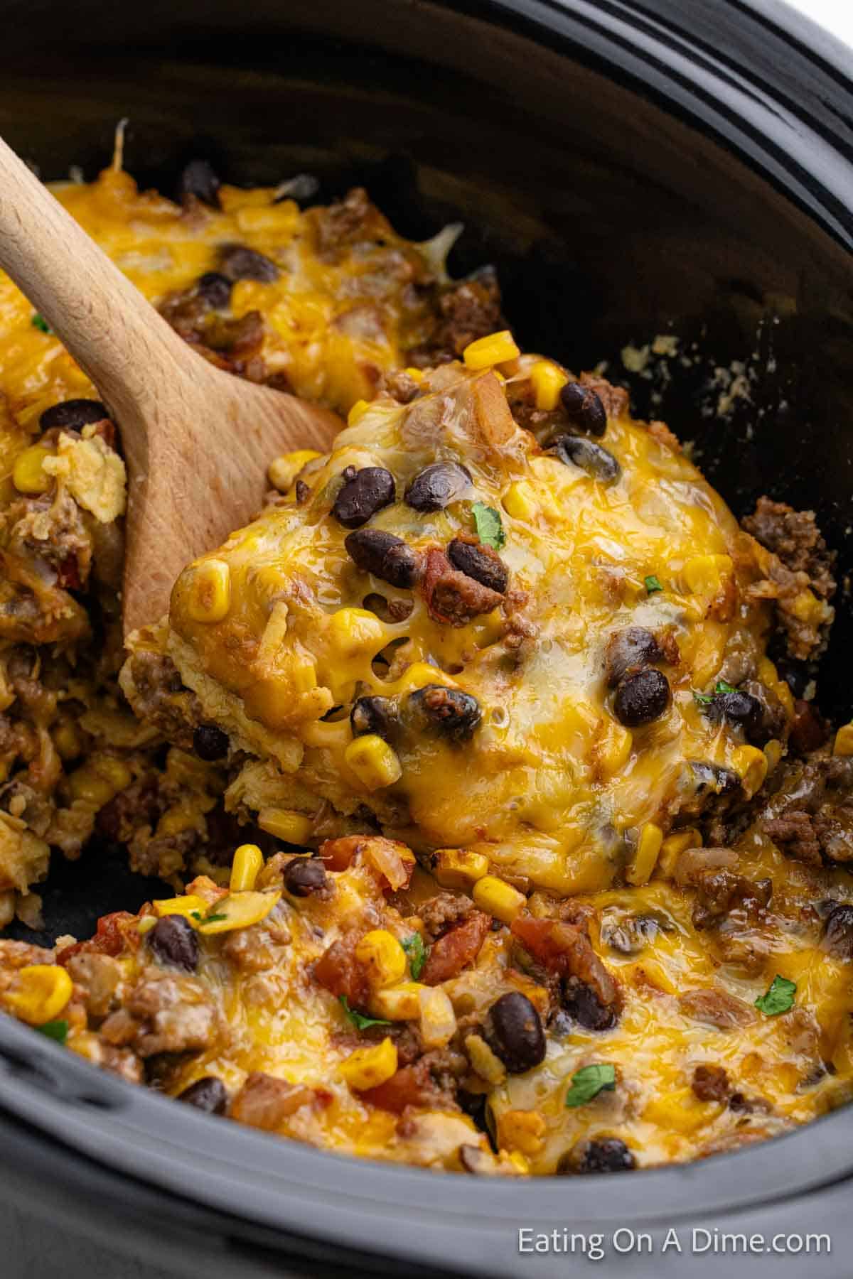 Mexican Lasagna in the slow cooker with a serving on a wooden spoon