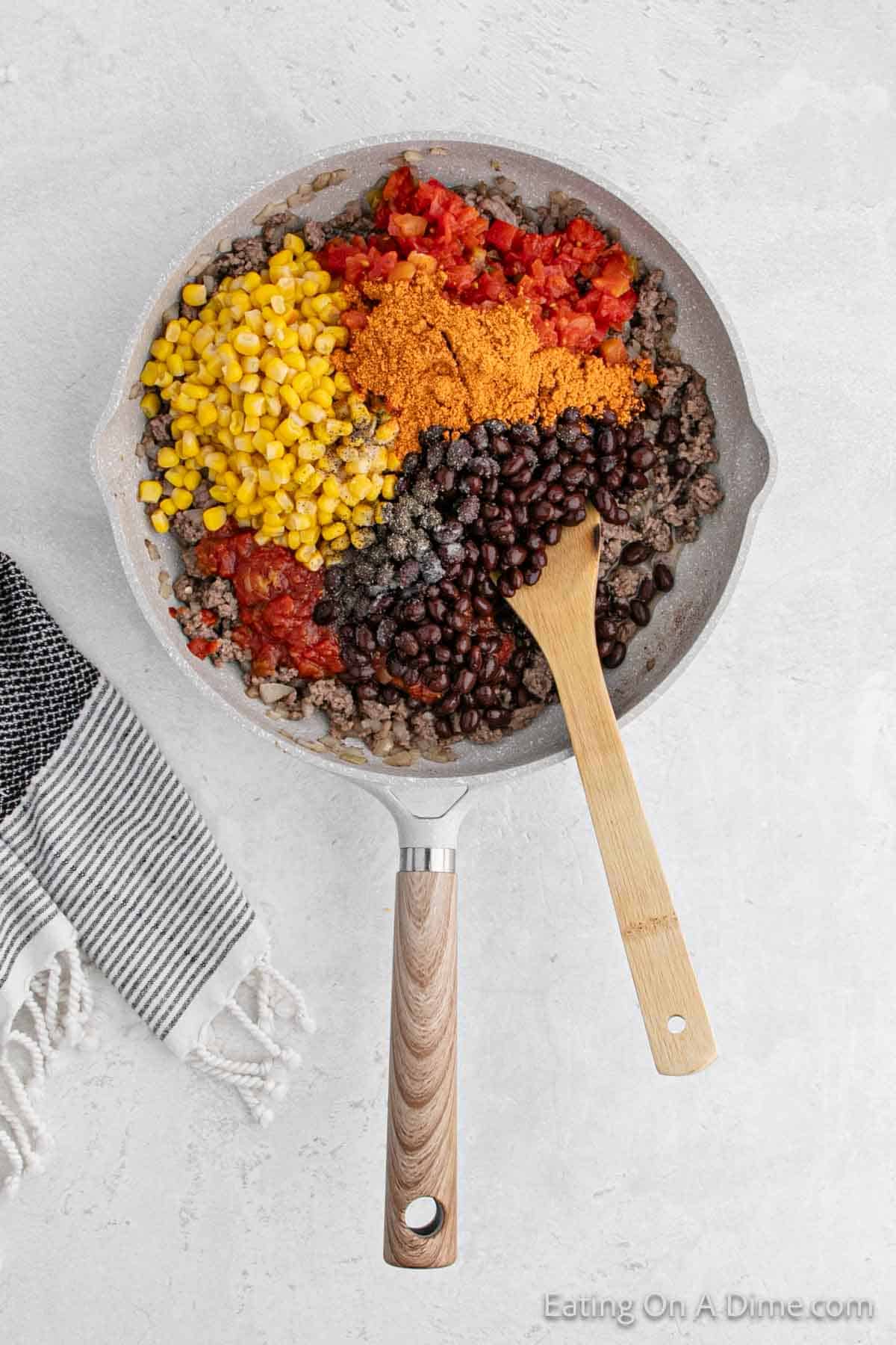 Combining the seasoning, beans, corn and salsa with the cooked meat in a skillet with a wooden spoon