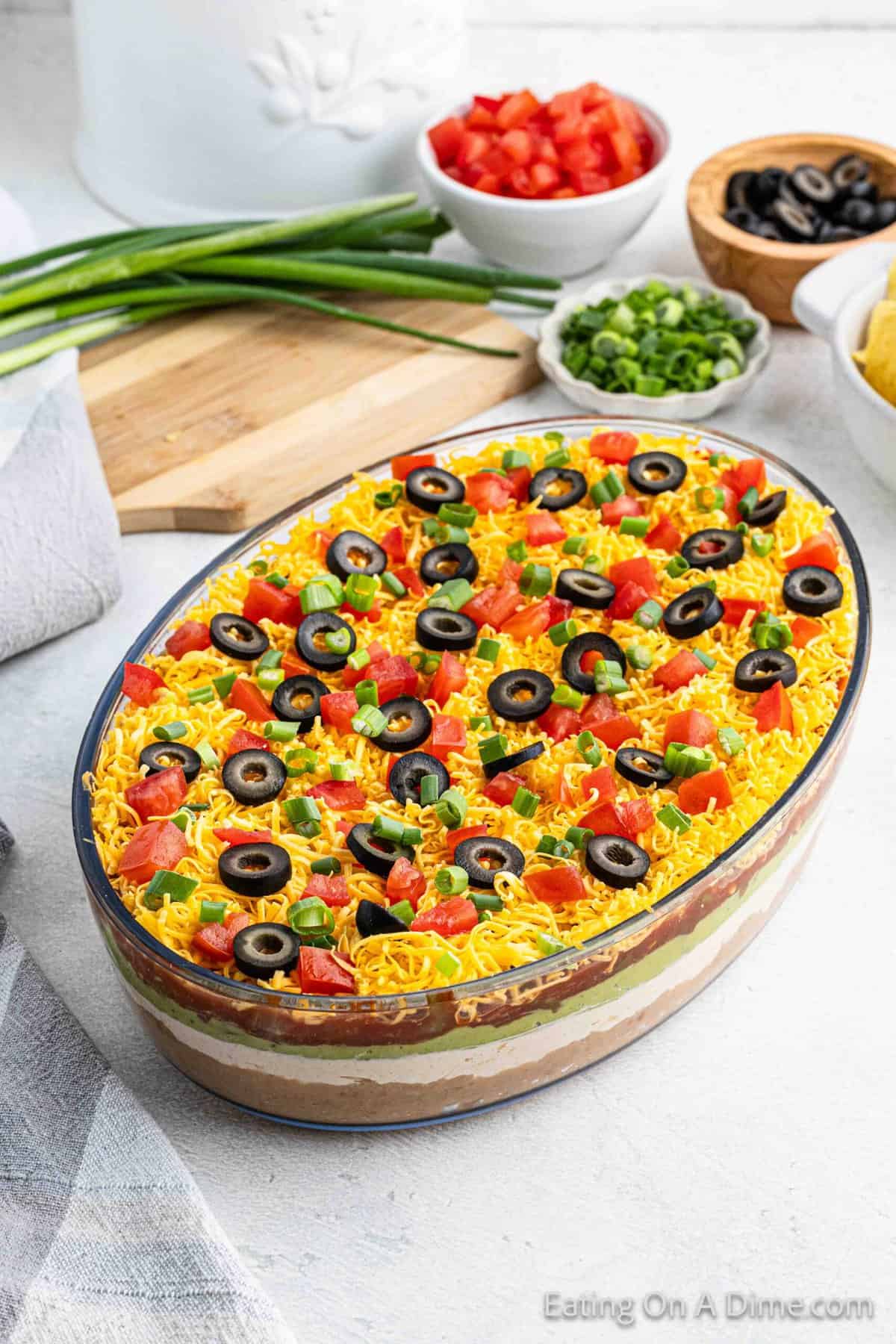 7 Layer Dip in a round clean dish topped with chopped tomatoes, slice black olives and chopped onions