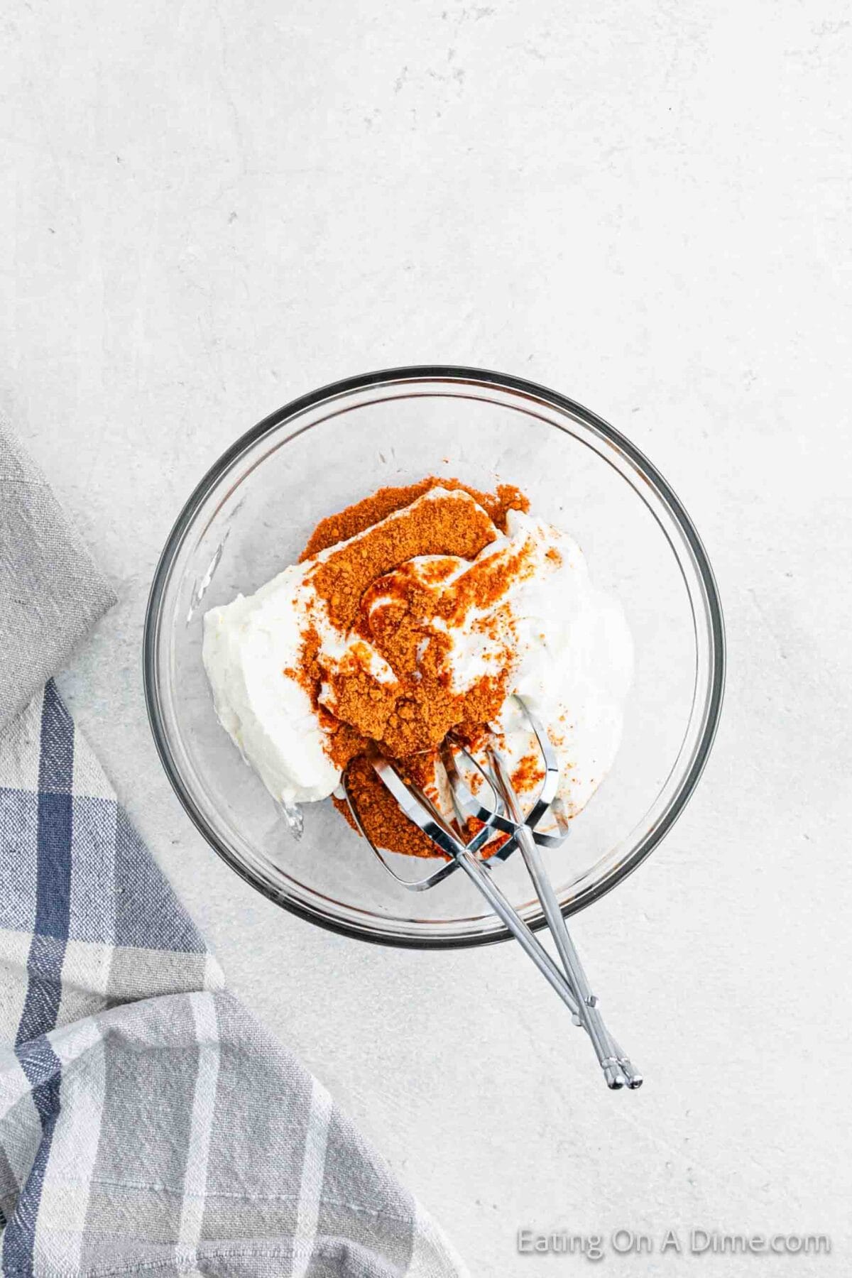 Cream Cheese, sour cream and taco seasoning in a clear bowl with hand mixer