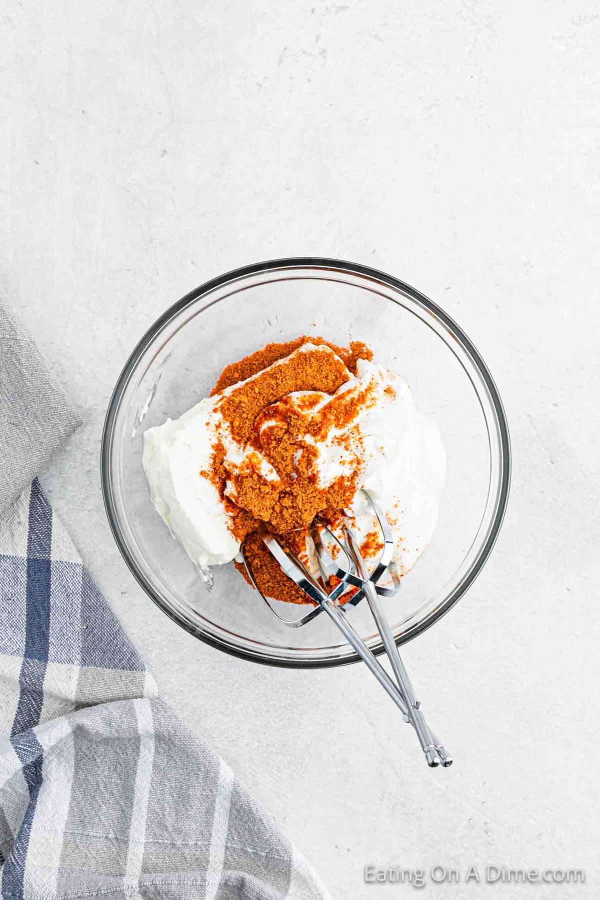 Cream Cheese, sour cream and taco seasoning in a clear bowl with hand mixer.