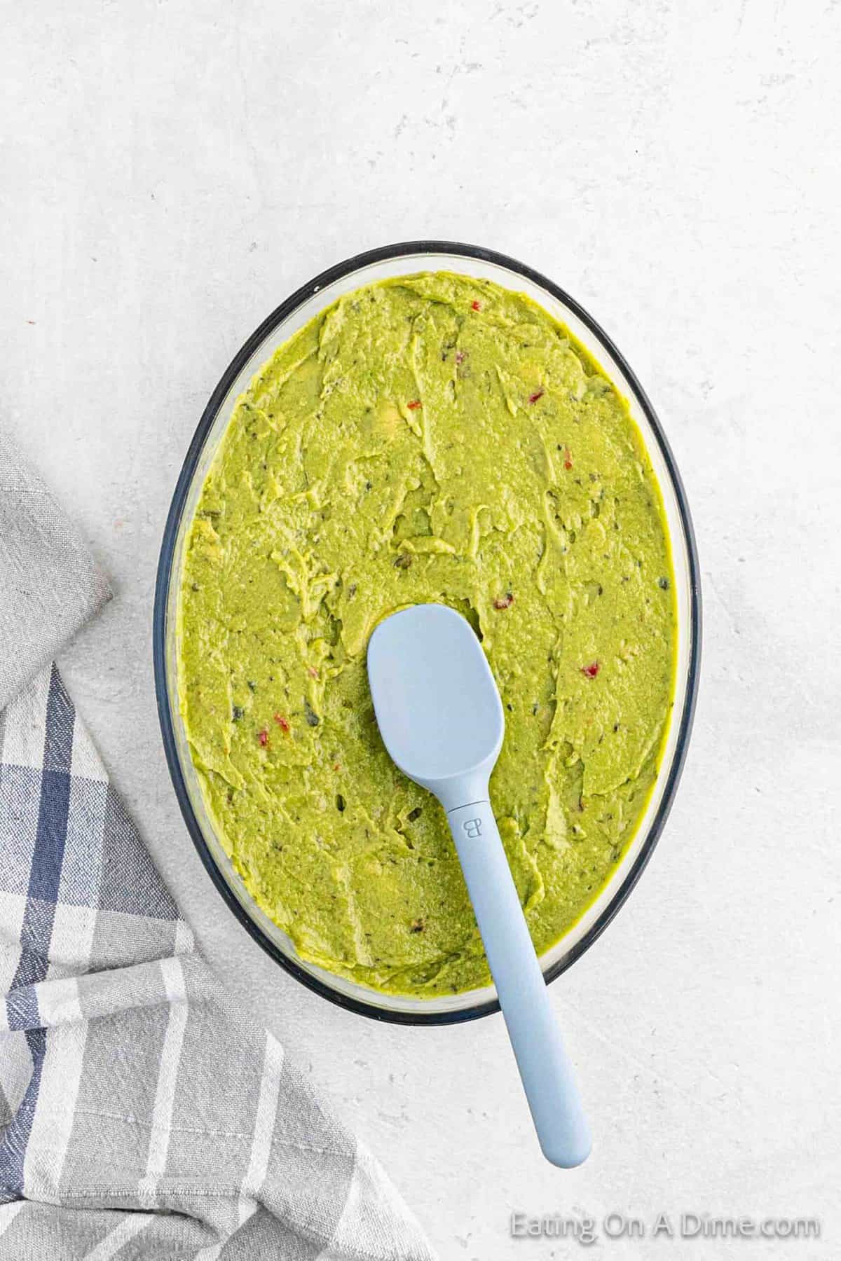 Guacamole spread into a clear dish with a spatula