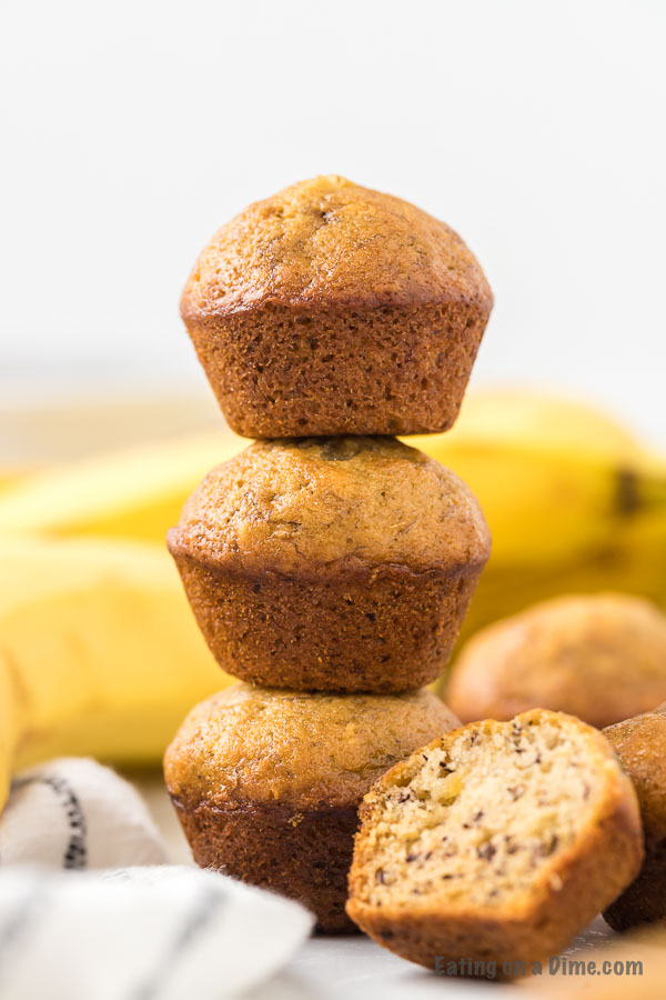 Mini Banana Bread Muffins stacked on top of each other with some bananas behind them. 
