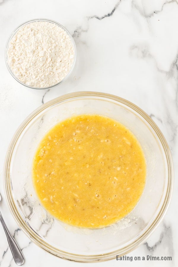 A bowl of flour on the side of a bowl of butter, egg, sugar, vanilla, baking soda, and salt