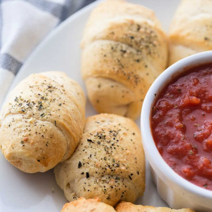 Pizza crescent rolls on a platter with a bowl of marinara sauce