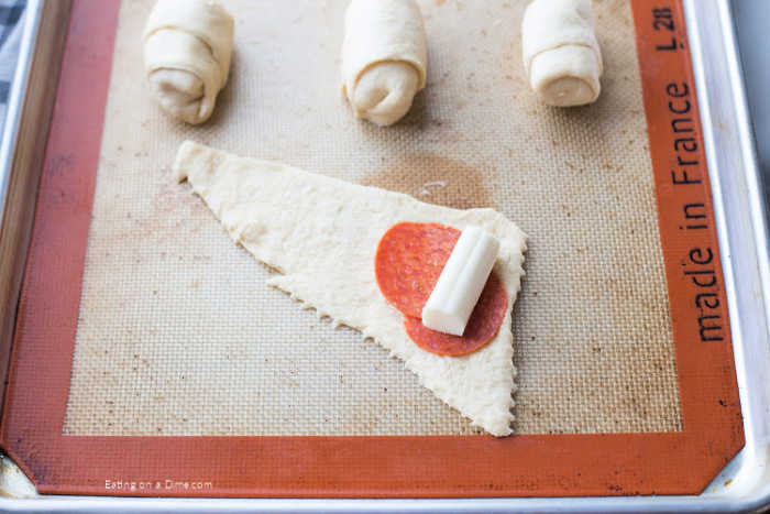 Placing the cheese and pepperoni in the crescent rolls and wrapping them up