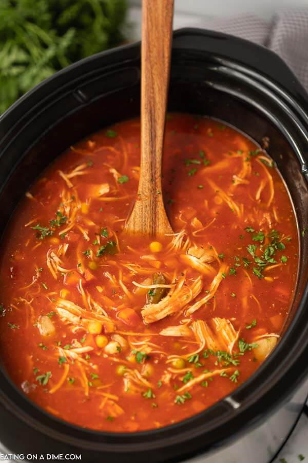 Overview of Chicken Vegetable Soup in a black crock pot with a wooden spoon in it. 