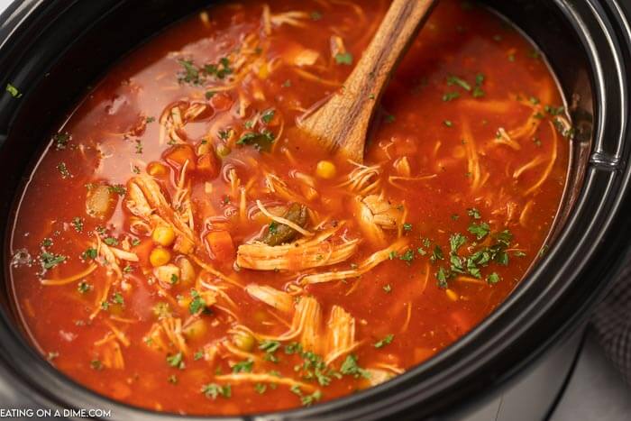 Close up of chicken vegetable soup in a crock pot with a wooden spoon in the middle of the crock pot.  