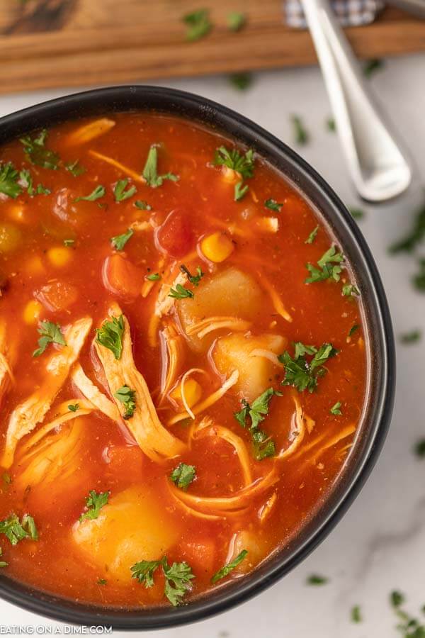 Close up of Chicken Vegetable Soup in a Black Bowl showing all the ingredients in the soup like chicken, potatoes, corn, tomatoes and peas.  