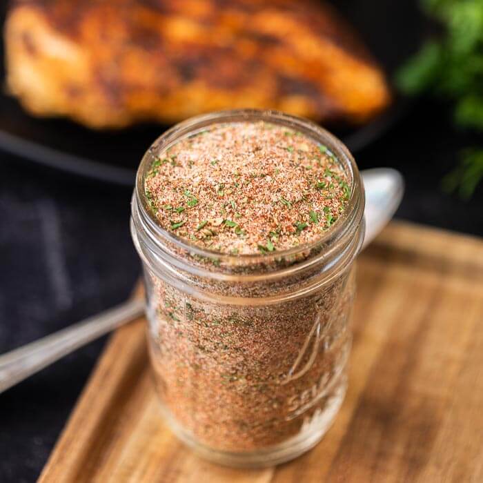 Close up of a jar of homemade blackened seasoning with chicken in the background.  