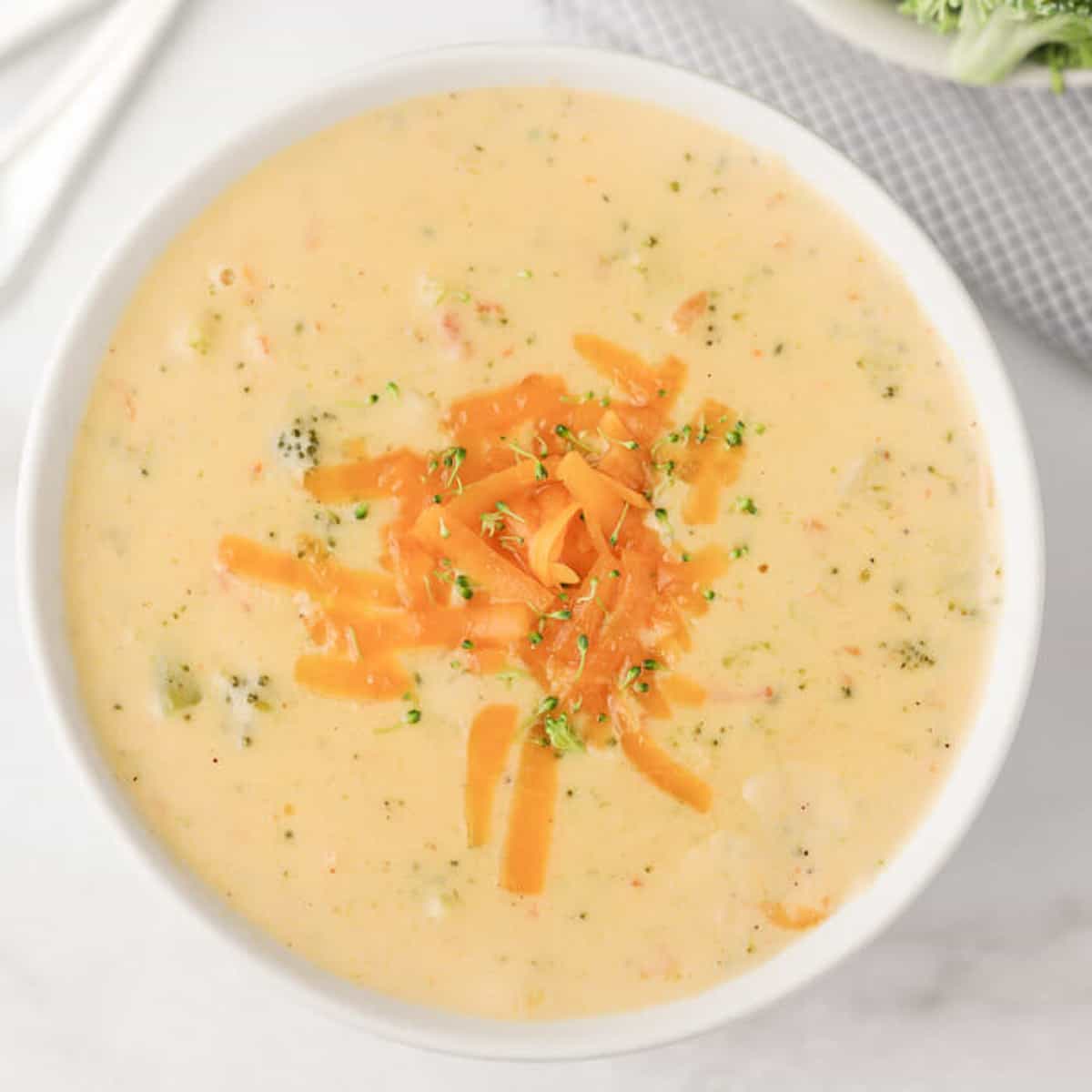 Close up of a large bowl of Panera Bread Broccoli Cheese Soup topped with shredded cheddar cheese.