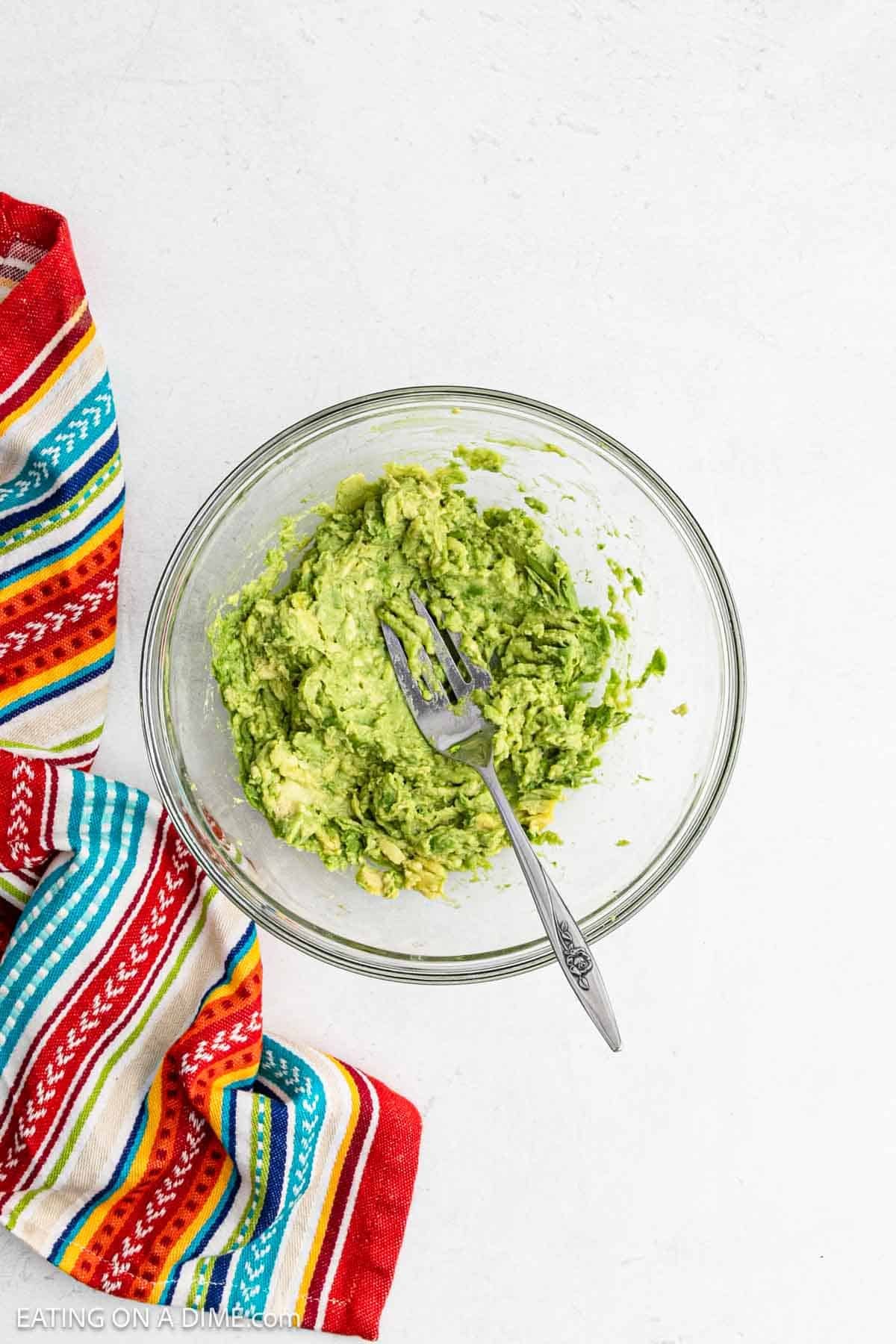 Mashed avocados in a bowl with a fork.